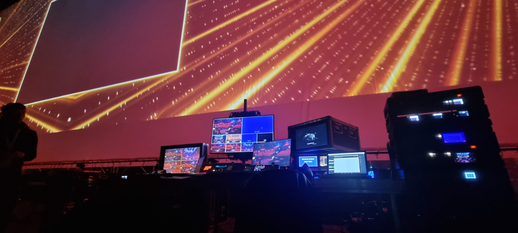 Régie vidéo installée sous les grills d’une salle de spectacle éclairée en ambre