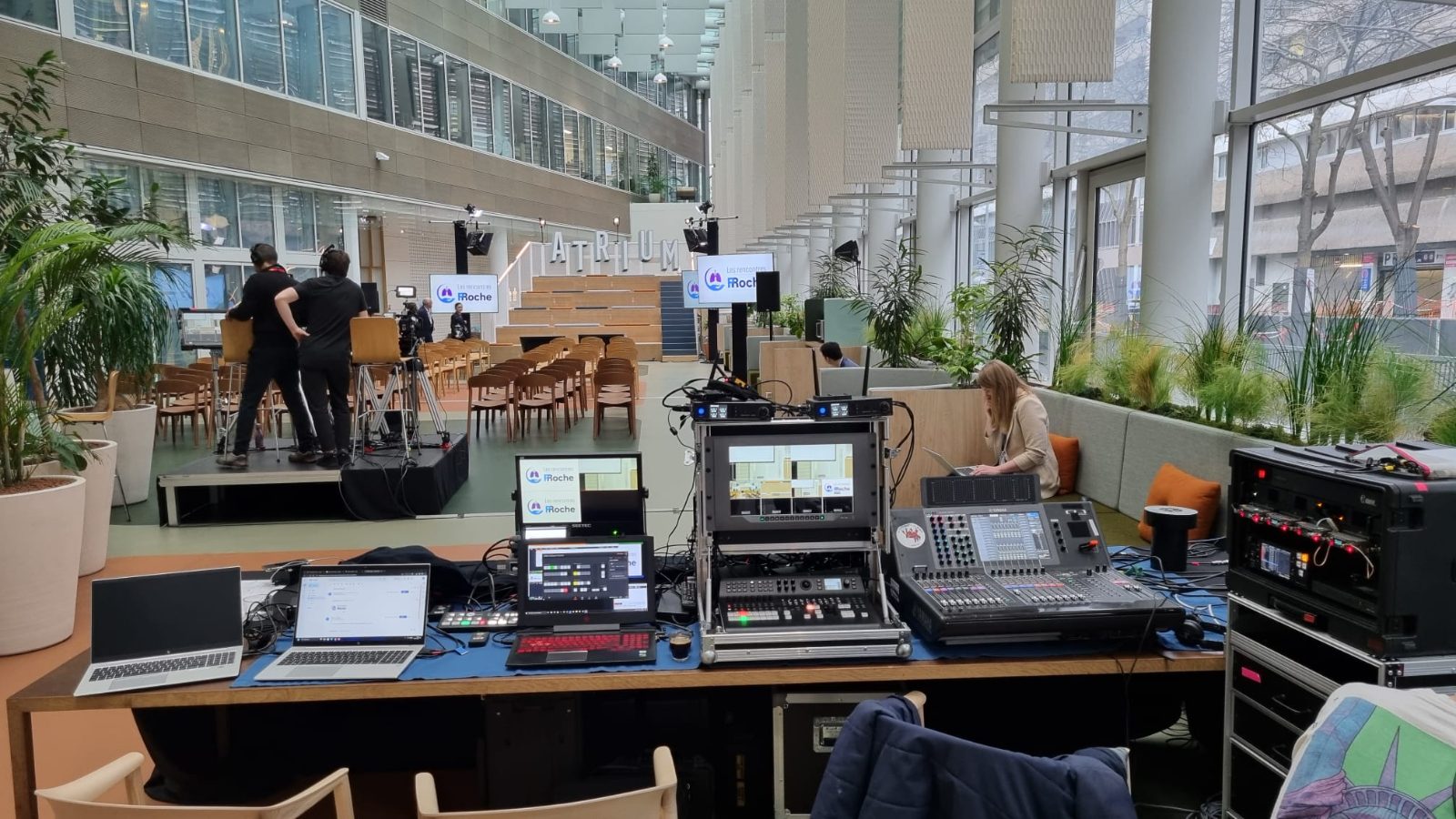 Régie son et vidéo installée en atrium, console de mixage, écrans de salle et plateau au fond
